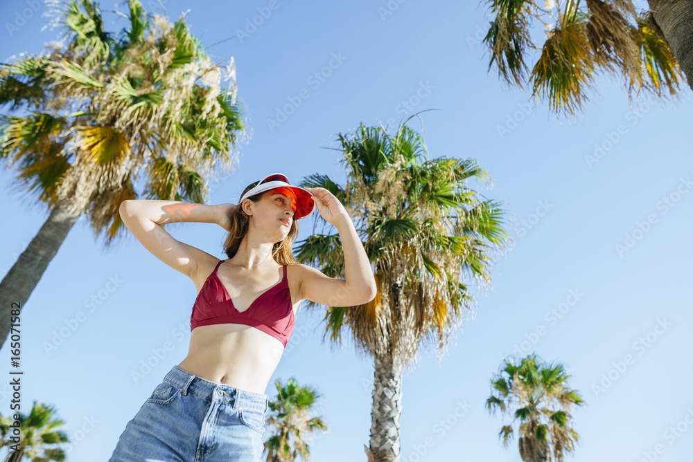 Portrait of young woman with bikini and sun visor with blue sky background and palm trees
