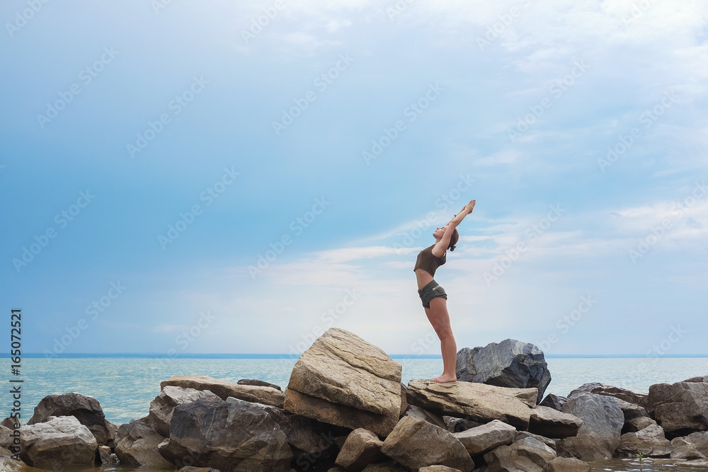 Pose greeting the sun. Girl practicing yoga against the blue sky. Woman raises her arms to the sky in the pose of namaste. Place to insert text.