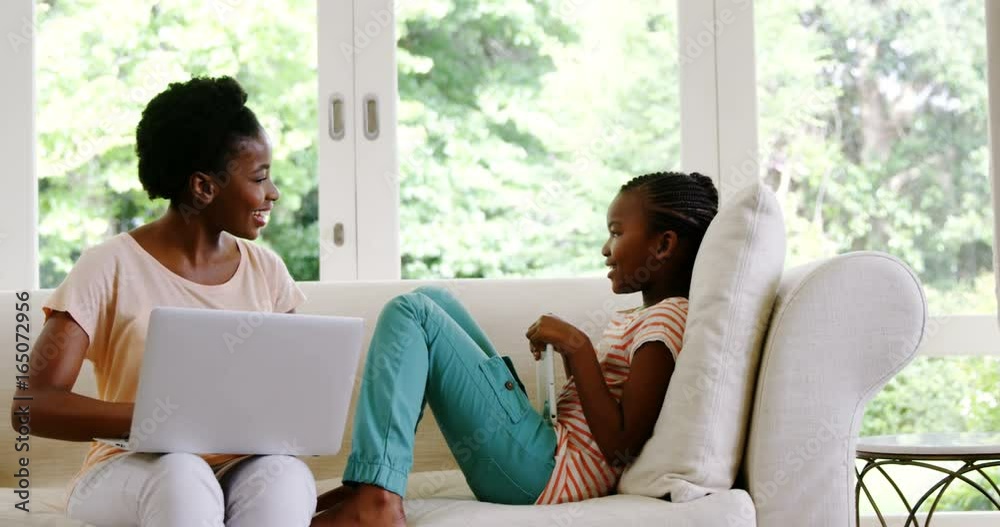 Mother and daughter using laptop and digital tablet in living room Mother and daughter using laptop and digital tablet in living room