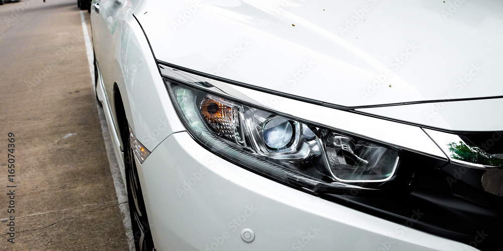 White car parked on the street,focused on headlamp.