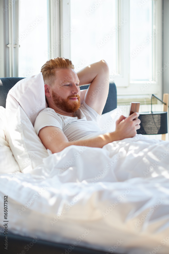Young man texting messages over mobile phone while lying in bed Young man texting messages over mobile phone while lying in bed