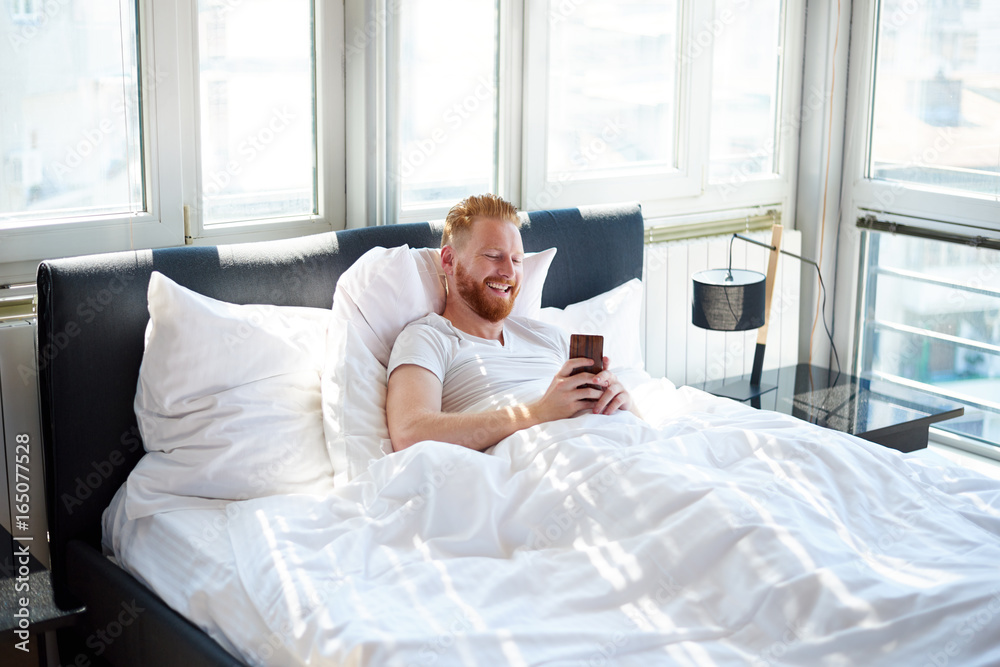 Young man texting messages over mobile phone while lying in bed Young man texting messages over mobile phone while lying in bed