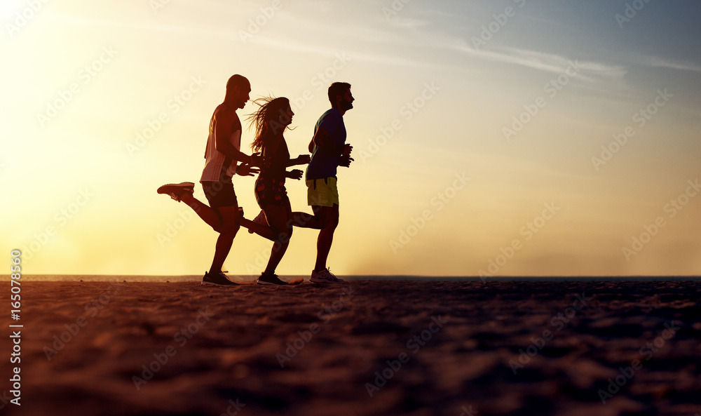 Group of young people running at the beach on beautiful summer sunset.