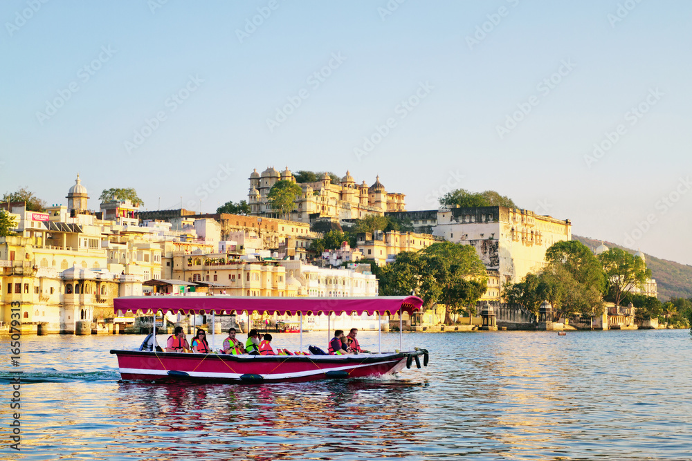 UDAIPUR, RAJASTHAN, INDIA - DECEMBER 8, 2011: Tourists on the boat taking Udaipur Lake Pichola sunset boat ride with City Palace on background
