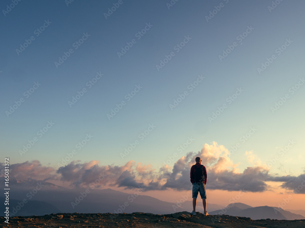 Fototapeta premium Man stands on top of a mountain and looks at the sunset
