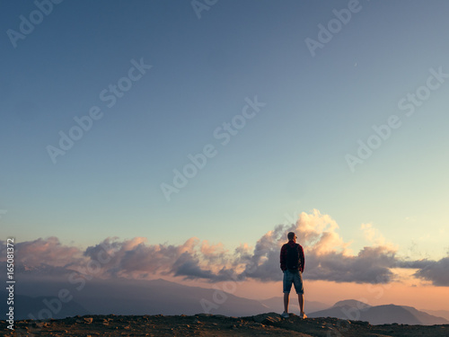Man stands on top of a mountain and looks at the sunset