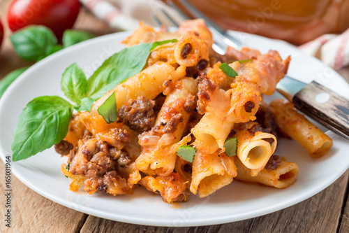 Ziti bolognese on white plate, pasta casserole with minced meat, tomato sauce and cheese, horizontal photo