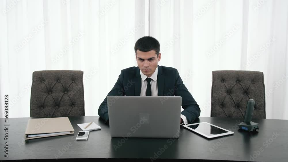 Portrait of Young handsome businessman working with laptop at desk in the modern office, with phone, unexpected obstacles, risky business, getting a second opinion from another entrepreneur Portrait of Young handsome businessman working with laptop at desk in the modern office, with phone, unexpected obstacles, risky business, getting a second opinion from another entrepreneur