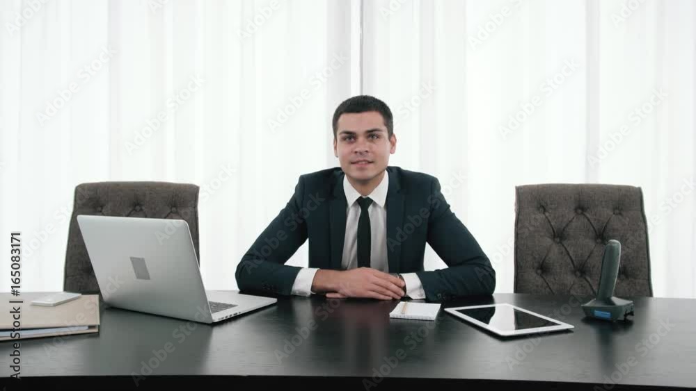 Happy businessman sitting in front of laptop and smile, portrait of young business man director in modern office Happy businessman sitting in front of laptop and smile, portrait of young business man director in modern office