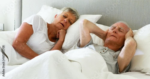 Senior man covering his ears while woman snoring in bedroom photo