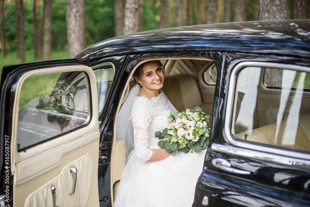 Beautiful bride in white wedding dress with bridal bouquet in the old black car Beautiful bride in white wedding dress with bridal bouquet in the old black car