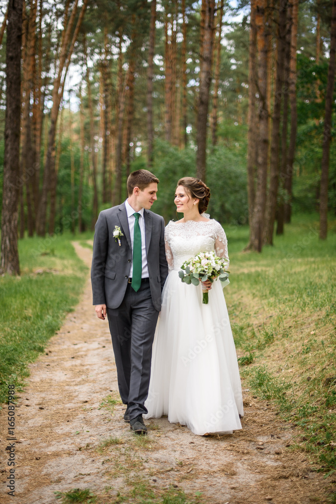 Just married loving couple in wedding dress and suit  in a forest. happy bride and groom walking  