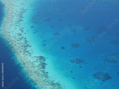 Aerial view of an atoll in Maldives with underwater coral reef seen through clear blue sea water. Maldives is a tropical island country in Indian Ocean consisted of more than a thousand islands.