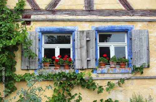 two old windows with shutters and red geraniums