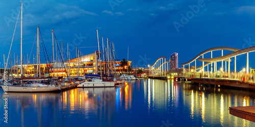 Photography Panorama with Port Vell marina and wavy wooden walkway known as the Rambla de Mar at night in Barcelona, Catalonia, Spain