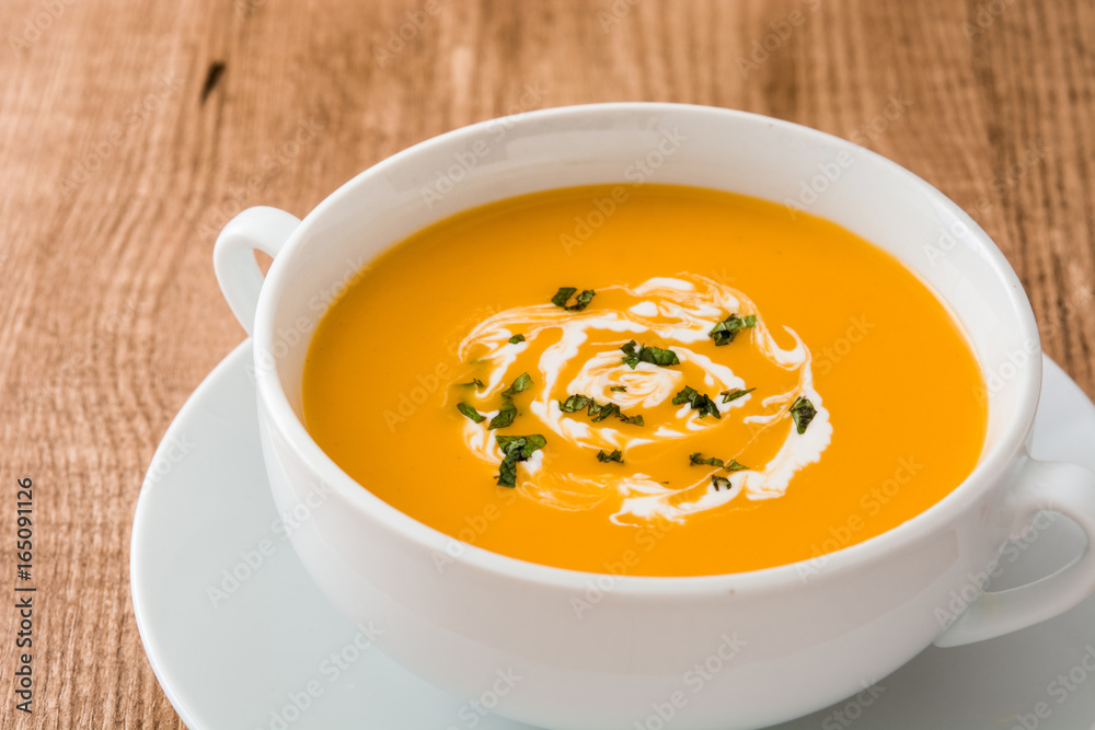 Pumpkin soup in white bowl on wooden table
