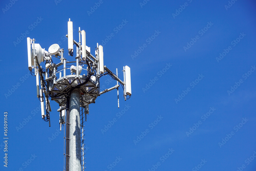 Top part of cell phone communication tower with multiple antennas against a blue sky