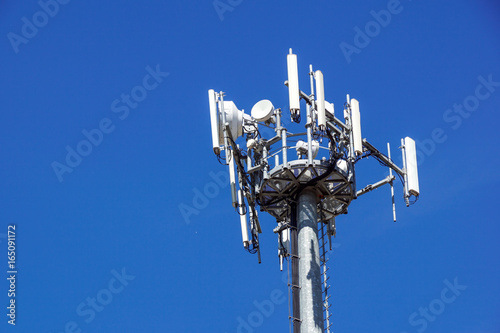 Top part of cell phone communication tower with multiple antennas against a blue sky