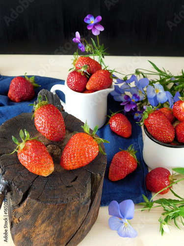 Fresh ripe strawberries on a stump and in the mugs. Flowers in the background