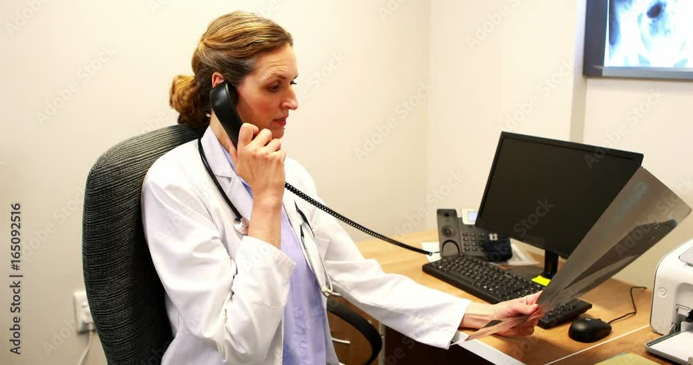 Female doctor examining an x-ray while talking on telephone Female doctor examining an x-ray while talking on telephone