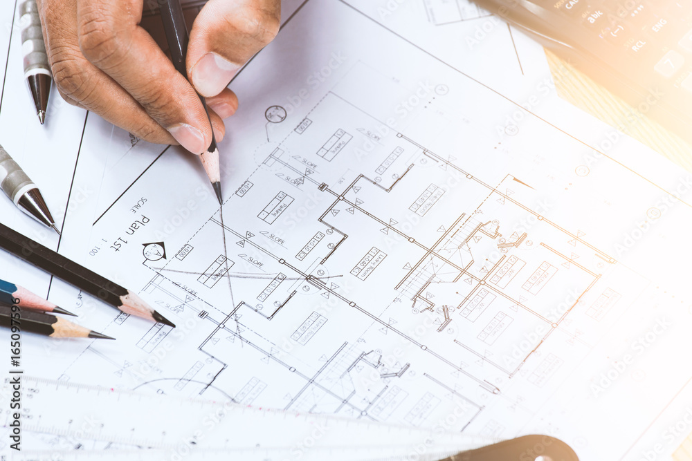 Close-up of young person hands marking on blue print with architect instrument at office desk. Close-up of young person hands marking on blue print with architect instrument at office desk.