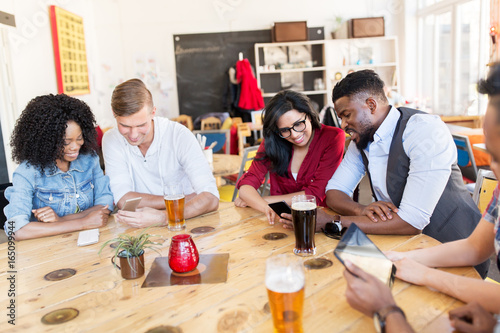 friends with smartphone, tablet pc and beer at bar