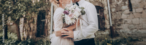 stylish wedding couple with bouquet. modern bride and groom holding fashionable bouquet at old  castle. fine art wedding photo, romantic moment, long edge photo