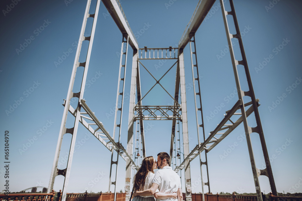 stylish couple in love hugging and kissing on bridge in the summer city. modern woman and man in fashionable white clothes relaxing on vacation at the river, space for text stylish couple in love hugging and kissing on bridge in the summer city. modern woman and man in fashionable white clothes relaxing on vacation at the river, space for text