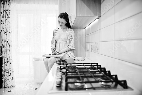 Happy young woman in pink robe sitting on the surface and making the salad. Black and white photo.