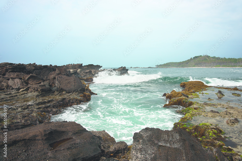 Blue ocean waves crashing and splashing against brown rocks on the coast.
