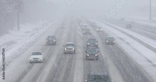 Cars driving in traffic on a snow covered road during a winter blizzard