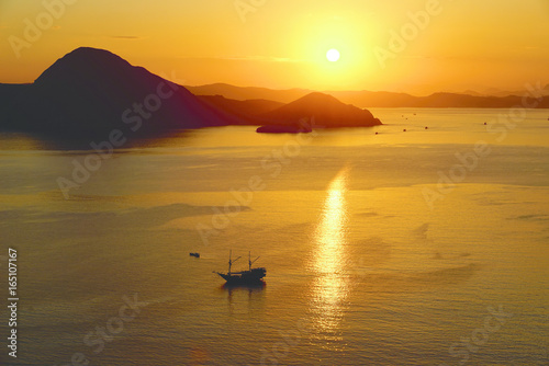Orange sunrise view from Padar Island part of komodo national park with little silhouette boat in the ocean, Flores Indonesia.