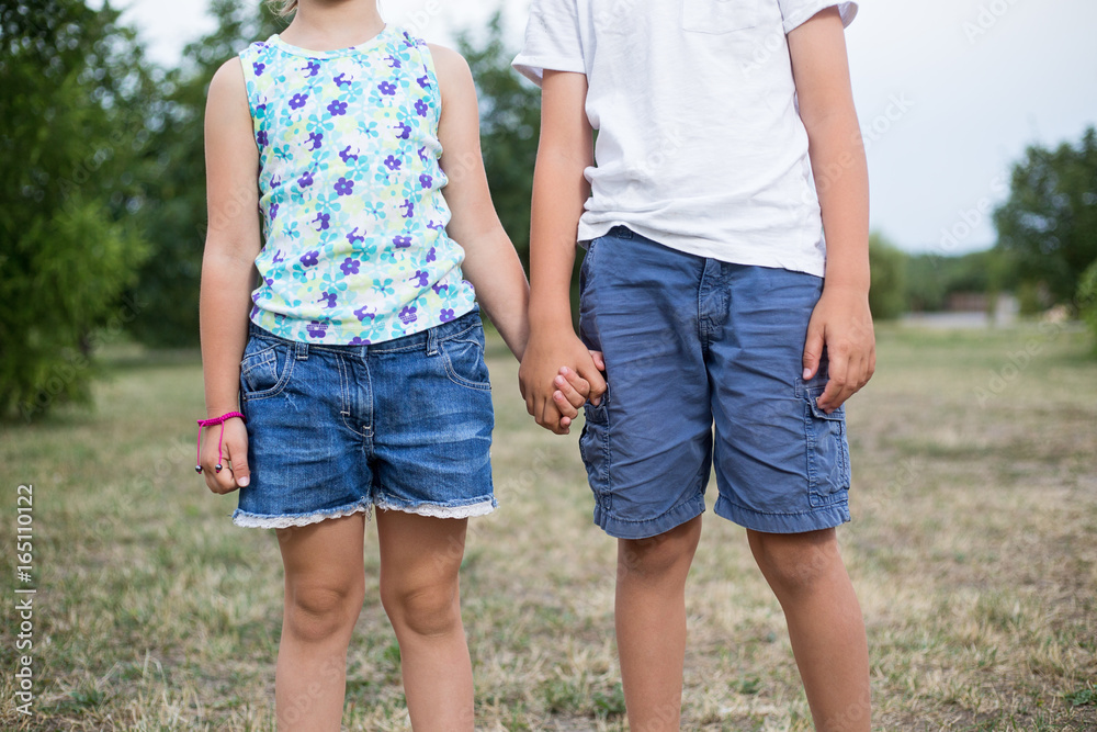 Two young caucasian kids holding hands outdoors on summer day