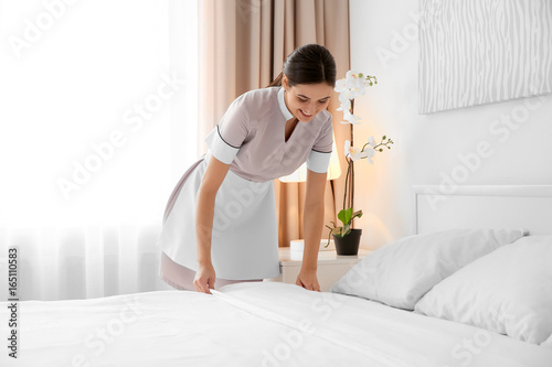 Young maid making bed in light hotel room photo