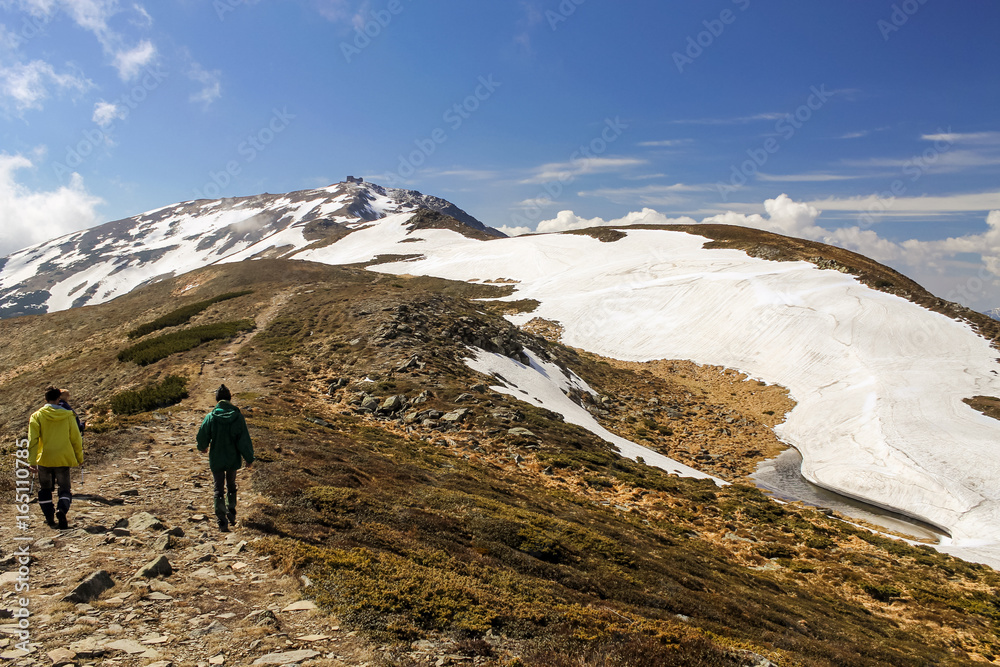 men hikers walking on mountain valley road way to the abandoned observatory during spring snow covering the hills