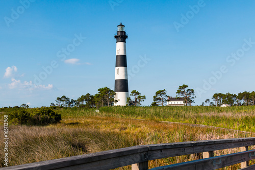 Bodie Island lighthouse and surrounding buildings on the Outer Banks of North Carolina near Nags Head, with wooden fencing in the foreground.