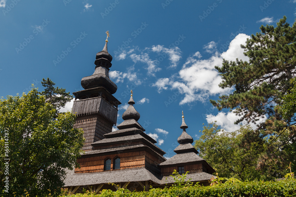 Old wooden Lemk church against a bright blue sky with clouds.