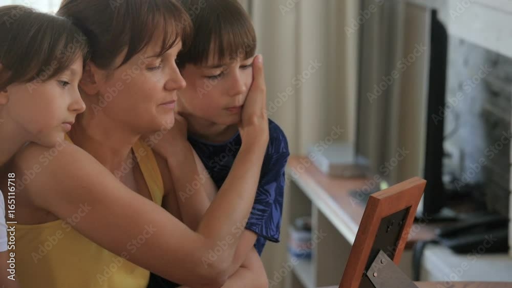 Sad family. Children are hugging sad mother. The girl looks at the photo with sadness. Sad mother. Kids look at stressed out mom.