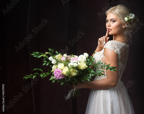 beautiful bride with a bouquet of flowers holds a finger to his mouth without giving away the secret
