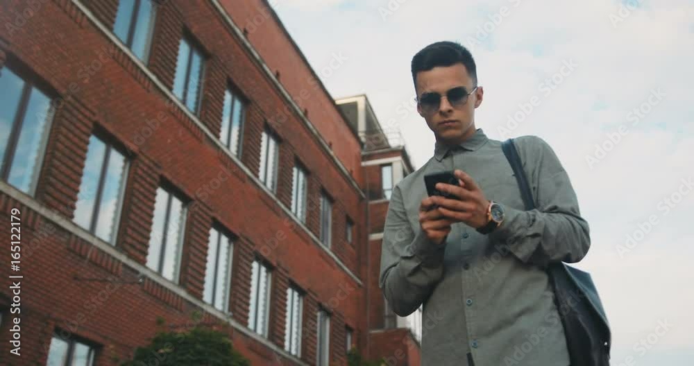 Young urban stylish boy guy man walking using phone smartphone street mobile app texting tapping wearing smart casual shirt city lifestyle building sunglasses student elegant clothing trendy hipster Young urban stylish boy guy man walking using phone smartphone street mobile app texting tapping wearing smart casual shirt city lifestyle building sunglasses student elegant clothing trendy hipster