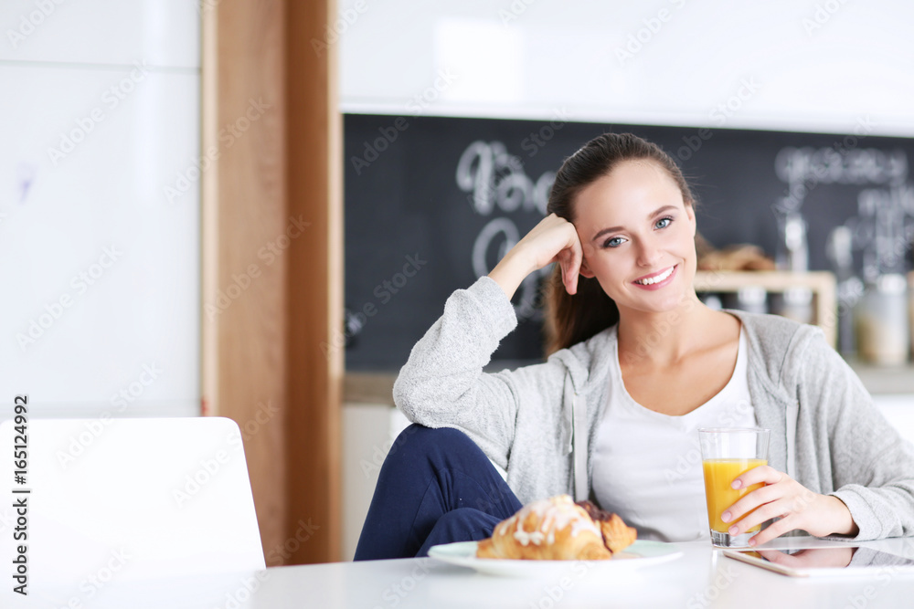 Young woman with orange juice and tablet in kitchen.