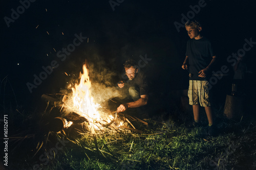 A man sticking tending campfire at night
