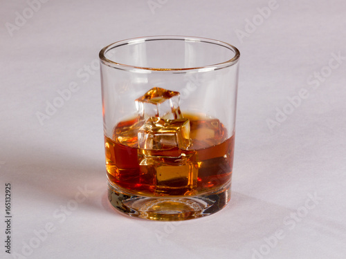 Glass of whiskey and ice on plain background