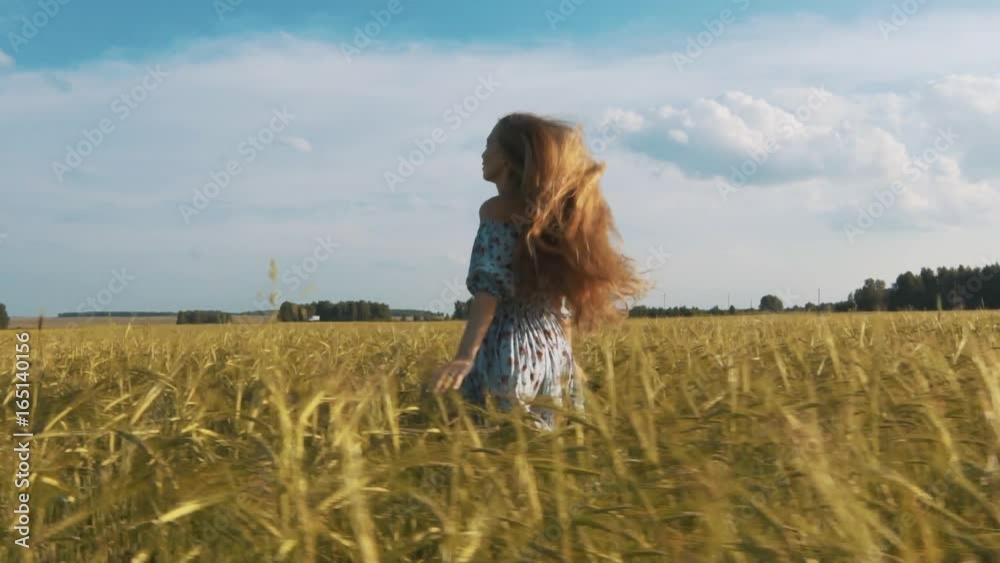 Beautiful healthy woman in dark dress with floral print stands in and then running across green field look back and wind blowing her hair Beautiful healthy woman in dark dress with floral print stands in and then running across green field look back and wind blowing her hair