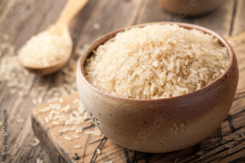 Uncooked parboiled rice in a bowl on wooden table photo