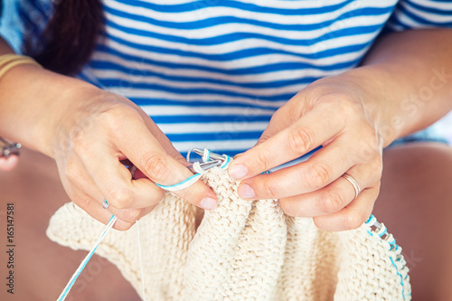 A young woman in a striped sweater knits a woolen white thread with knitting needles, a sweater, a top view