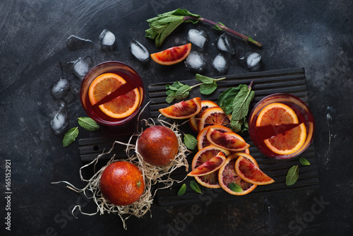 Fototapeta Naklejka Na Ścianę i Meble -  Juice of blood oranges with whole and sliced oranges on a dark metal background, view from above