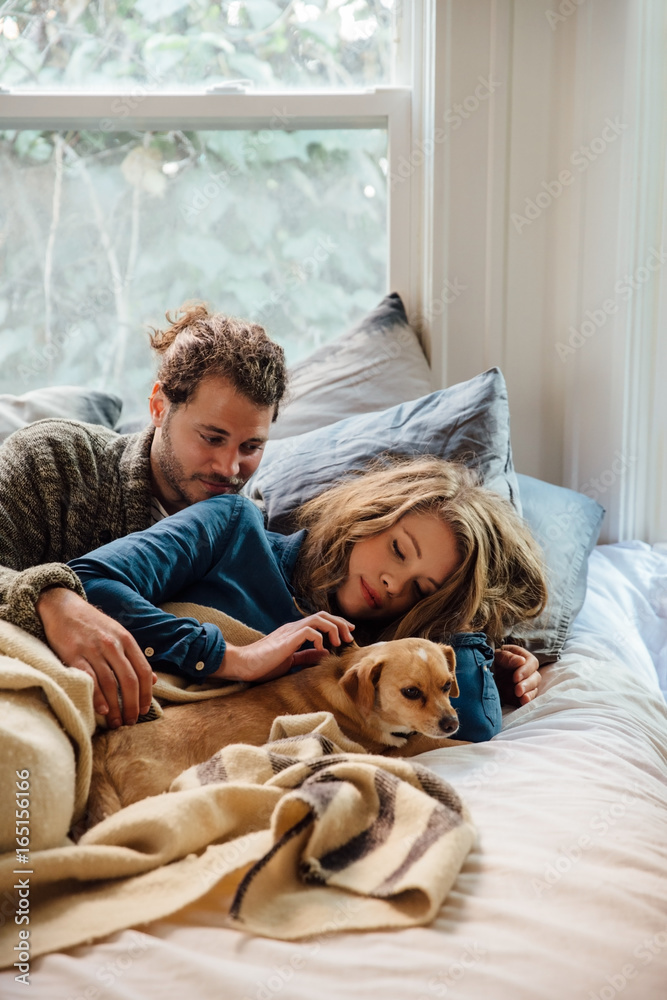 Couple relaxing on bed with their dog Couple relaxing on bed with their dog
