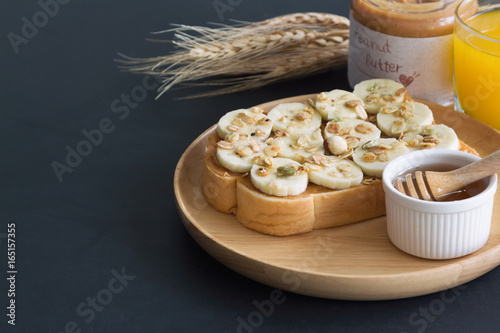 Banana peanut butter toast sandwich on wood plate with honey. Homemade open sandwich spread with peanut butter on top with banana slice and granola. Delicious healthy sandwich for breakfast or lunch.