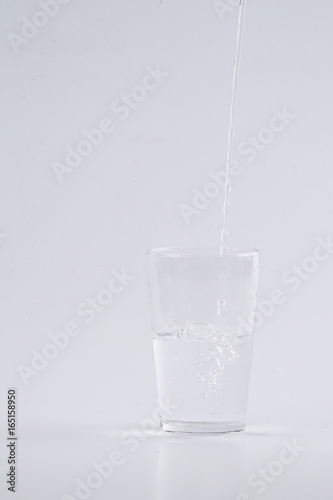 Water pouring into clear glass over white background